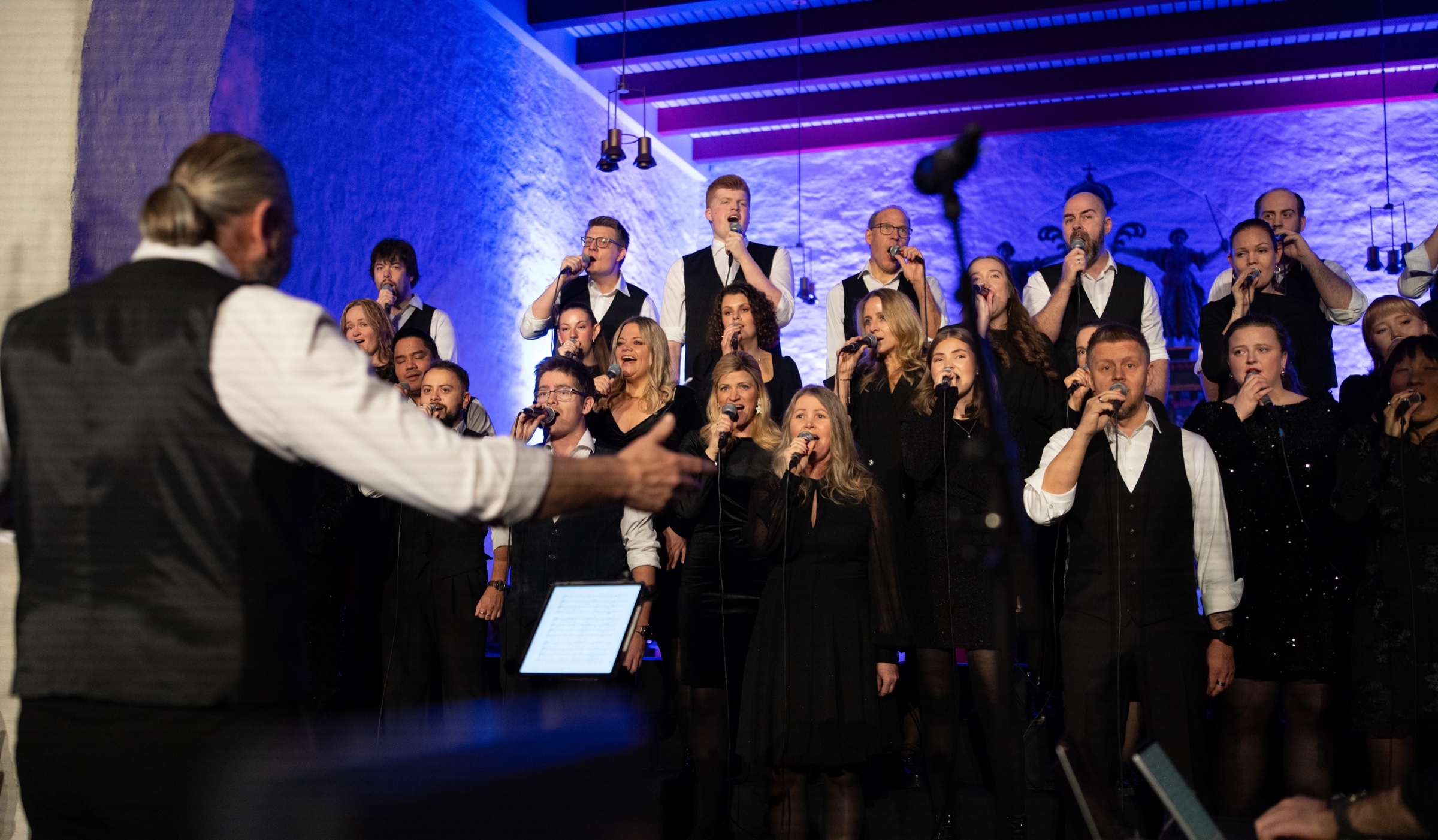 Dirigenten leder sangerne i The Real Choir under konsert